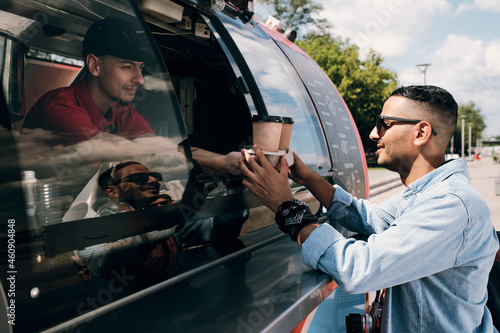 Guy in casualwear and sunglasses buying two drinks in street food truck on summer day