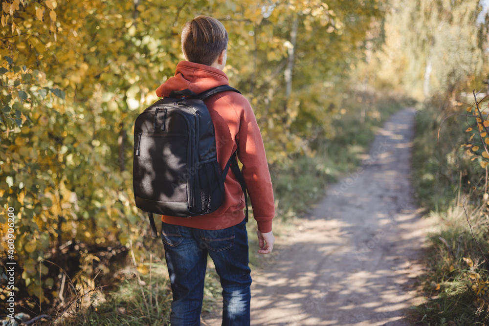 Teenager boy with backpack walking on path in autumn park. Active lifestyle, Back to school. Student boy in fall forest. People from behind Teenager boy with backpack walking on path in autumn park. Active lifestyle, Back to school. Student boy in fall forest. People from behind