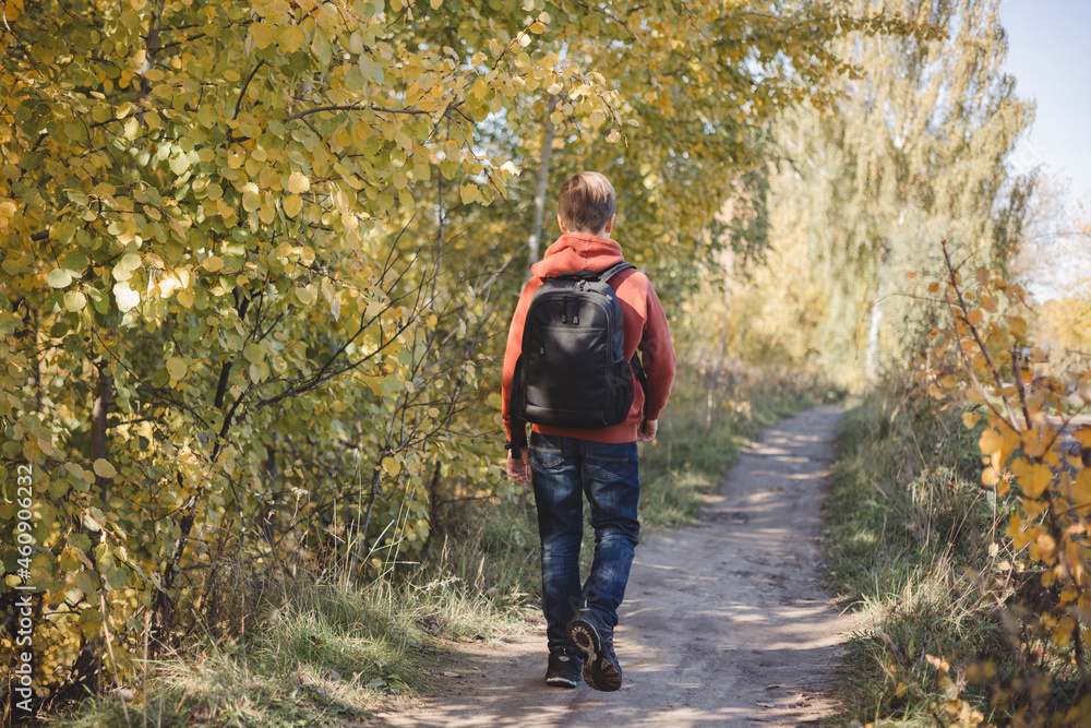 Teenager boy with backpack walking on path in autumn park. Active lifestyle, Back to school. Student boy in fall forest. People from behind Teenager boy with backpack walking on path in autumn park. Active lifestyle, Back to school. Student boy in fall forest. People from behind