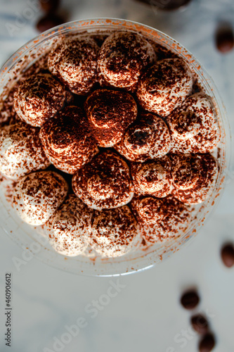 Perfect freshly made Italian tiramisu with cacao. Tiramisu portion on a white marble background. Delicious no bake tiramisu ready-to-eat. Delivery. A plastic cup restaurant dish delivery