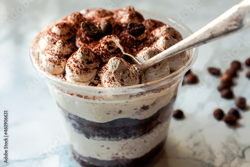 Served Italian dessert Tiramisu, cream, cocoa powder in a plastic take away cup. restaurant dish delivery..Close up.Selective focus