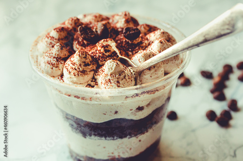 Served Italian dessert Tiramisu, cream, cocoa powder in a plastic take away cup.Healthy food and diet concept, restaurant dish delivery. Tone
