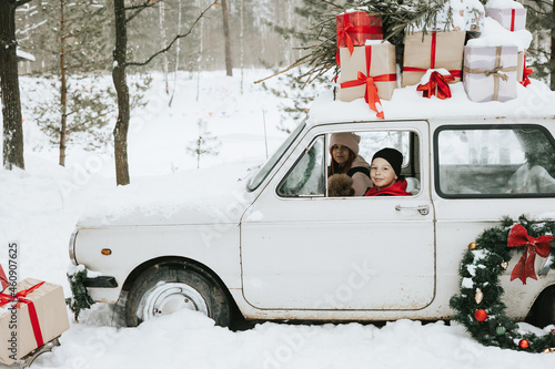 Children boy and girl with a dog driving a retro car decorated for Christmas among the winter forest in the village, the concept of a family Christmas and winter holidays