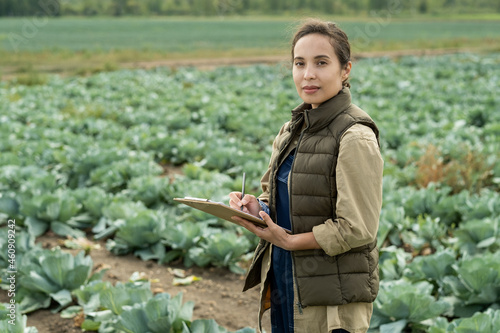Young confident female farmer making notes in document against cabbage field photo