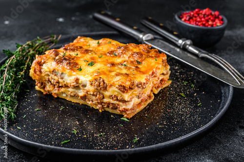 Lasagna with mince beef meat and tomato bolognese sauce on a plate. Black background. Top view