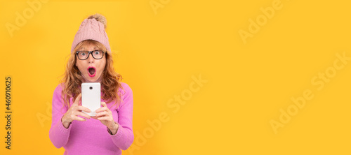 woman isolated on background wearing winter clothes looking surprised at mobile phone, space for text
