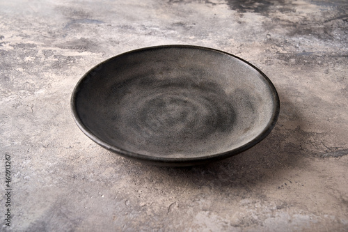 Empty dark deep plate on gray textured background as concrete. Close up, copy space