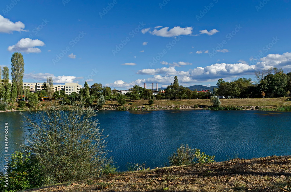 Fototapeta premium Autumn panorama of part of the neighborhood by the lake with green trees, shrubs and sunburned grass, Drujba, Sofia, Bulgaria