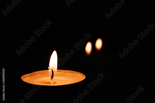 Close-up of burning tea candle in the dark. Reflection of candlelight flame.