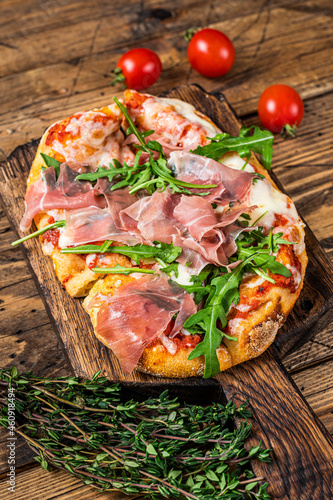 Sliced pizza with prosciutto parma ham, arugula and parmesan cheese on a wooden board. wooden background. Top view