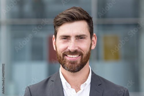 Boss man looking at camera and smiling, young businessman banker with beard photo with close up portrait