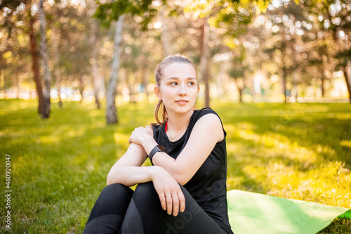 Fototapeta Naklejka Na Ścianę i Meble -  Attractive girl in sports uniform posing while sitting on a green fitness mat in the park.