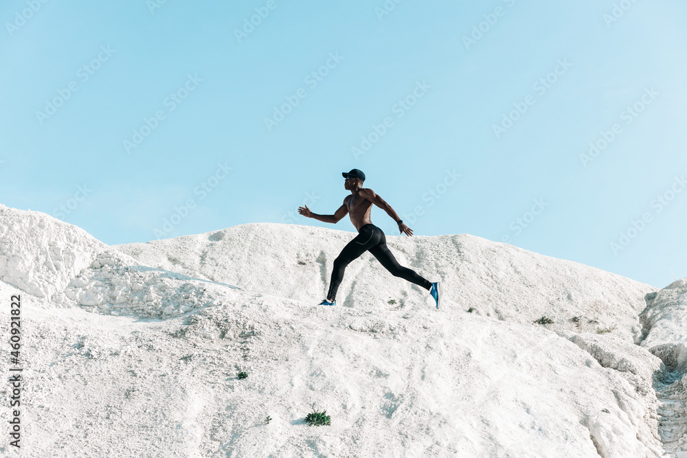 African athlete, silhouette against the sky at sunrise while running in the mountains along a steep path