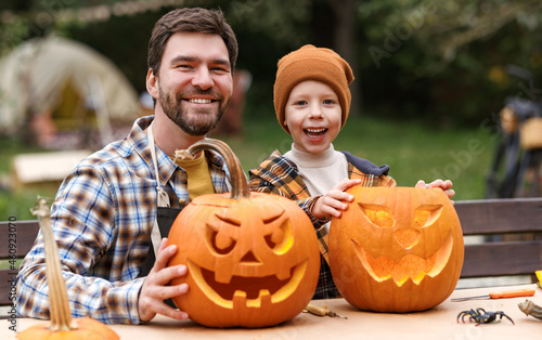 Smiling father and little boy son carving pumpkins in backyard photo