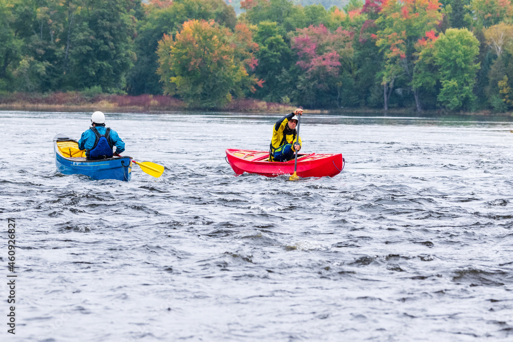 Two canoeists practice paddle strokes on a rainy fall day during a “moving water” paddling course.  At Palmer Rapids on the Madawaska River an iconic paddling destination in Eastern Ontario, Canada