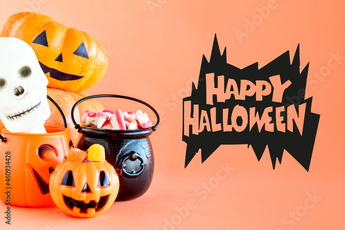 Happy Halloween decoration. Pumpkin, cauldron and gummy candies on orange background.