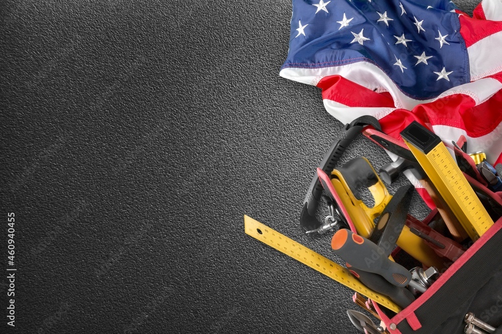 Happy Labor day concept. American flag with different construction tools on dark stone background, with copy space for text.