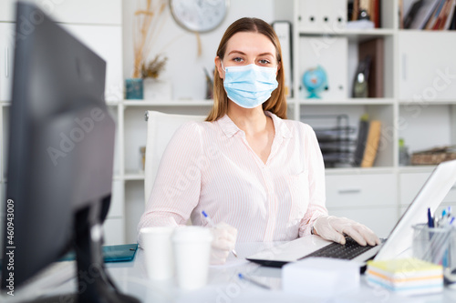 Businesswoman in protective mask working alone with laptop and papers in office, new normal due to coronavirus outbreak