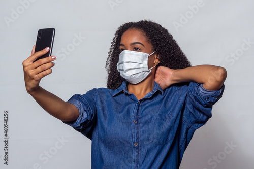 Mulher negra com cabelos cacheados usando máscara contra covid e usando o celular