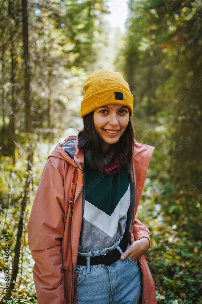 Portrait of smiling caucasian girl in yellow hat and pink raincoat in the sunny forest. A walk in the fresh air in a dense woods. Harmony of human and nature Portrait of smiling caucasian girl in yellow hat and pink raincoat in the sunny forest. A walk in the fresh air in a dense woods. Harmony of human and nature