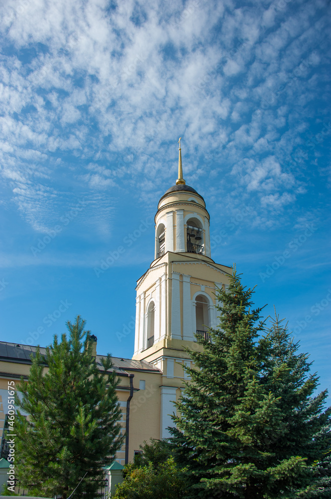 The bell tower of the church against the sky and fir trees