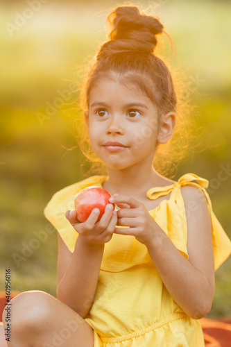 Funny swarthy little girl is eating an apple in the garden. Kid eat fruit outdoors. GMO free food. Healthy snack for children. summer concept. place for text. High quality photo