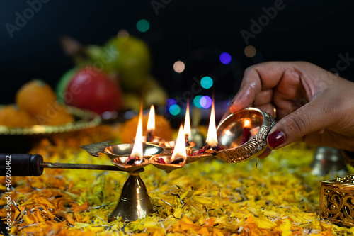 Panchmukhi Golden Brass Oil Diya Deep Being Lit By Girl Hands On Flower Bed Decoration And Bokeh Effect For Diwali Puja New Year Deepawali Or Shubh Deepavali Navratra Pooja Festival Celebration photo