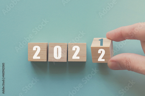 Hand flipping over wooden block of 2021 to 2022, New Year Resolutions, business concept