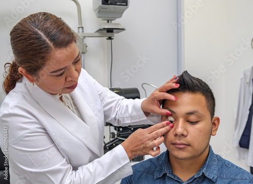 Latina woman ophthalmologist places a contact lens in the eye of a Latino patient in a specialized medical office