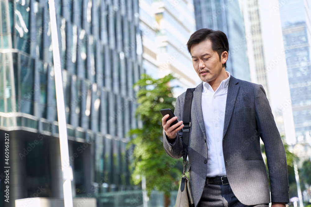 asian corporate executive looking at cellphone while walking in street