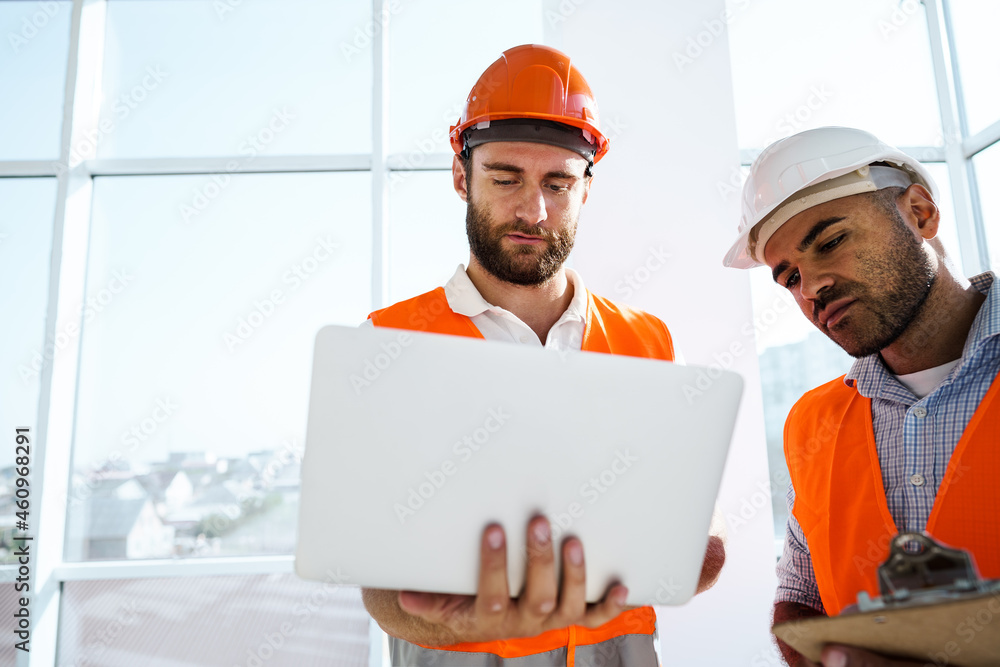 Two specialists supervisors in hardhats using laptop at construction site for work Two specialists supervisors in hardhats using laptop at construction site for work