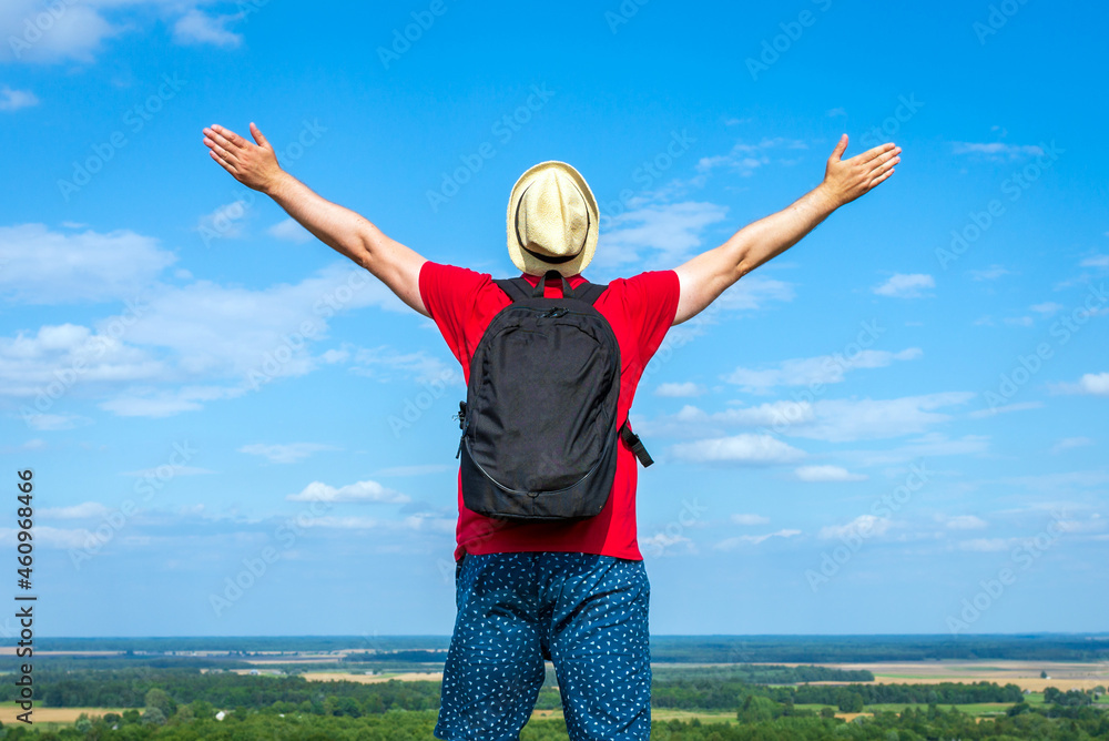 Tourist man with backpack enjoying the view in nature.Traveler man with backpack,arms outstretched stand on blue sky. Tourist man with backpack enjoying the view in nature.Traveler man with backpack,arms outstretched stand on blue sky.