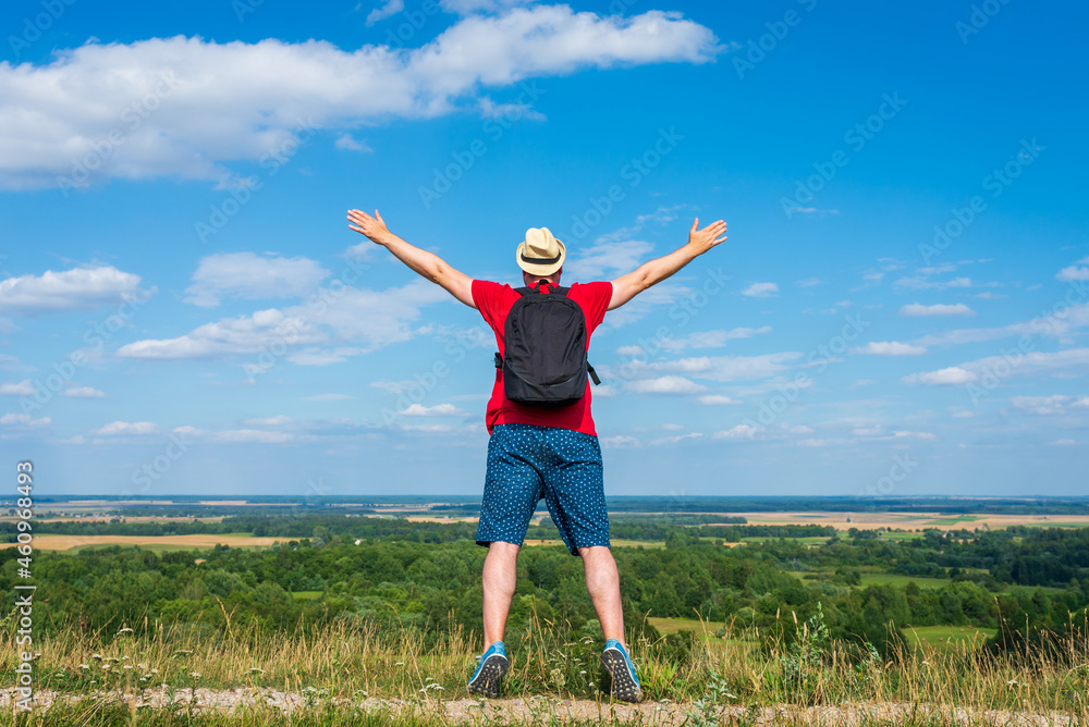 Tourist man with backpack enjoying the view in nature.Traveler man with backpack,arms outstretched stand on blue sky. Tourist man with backpack enjoying the view in nature.Traveler man with backpack,arms outstretched stand on blue sky.