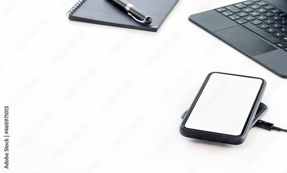 Mockup blank screen smartphone on charging station, tablet keyboard and notebook on white background. Mockup blank screen smartphone on charging station, tablet keyboard and notebook on white background.