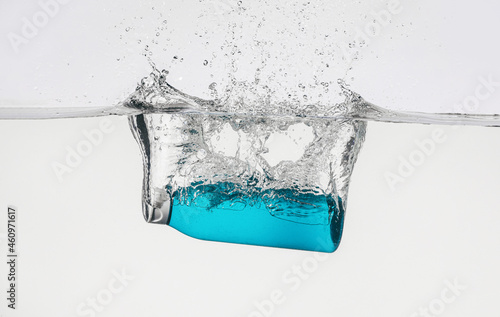 Bottle of cosmetic product in water with splashes on white background © Pixel-Shot