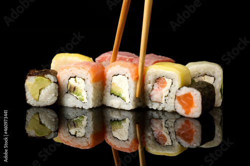 Wooden chopsticks taking delicious sushi roll on dark background