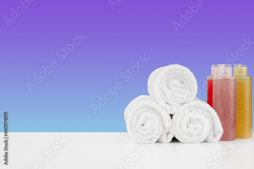 Pile of towels, bottles with shampoo on white table