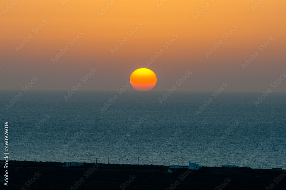 The sun sets behind the horizon line on the sea