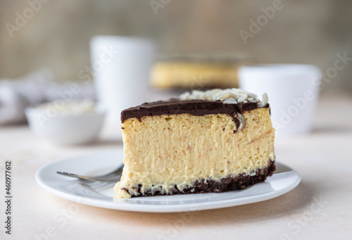 Slice of no baked creamy cheesecake with chocolate glaze and almond, light concrete background.