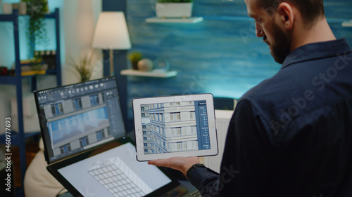 Architect holding digital tablet with building model for construction layout in office. Man engineer working on blueprint plan with touch screen monitor and device for architectural project