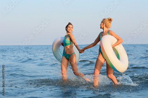 Beautiful young women with inflatable rings on sea beach