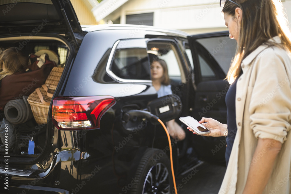 Portrait of mother, father and two daughters standing by car at electric vehicle charging station Portrait of mother, father and two daughters standing by car at electric vehicle charging station