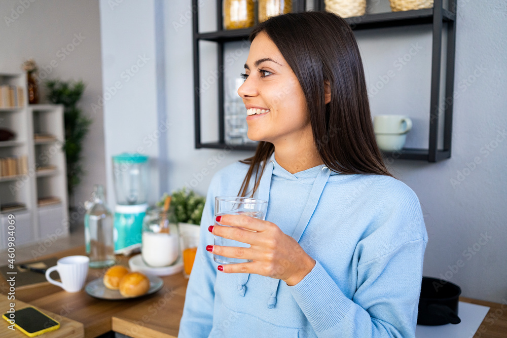 Smiling young woman holding glass of water at home Smiling young woman holding glass of water at home