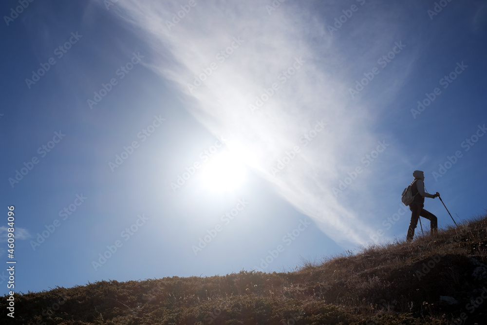 Young woman hiker with backpack on top of mountain on background of blue sky. Walk in the clouds. Discovery Travel Direction Concept