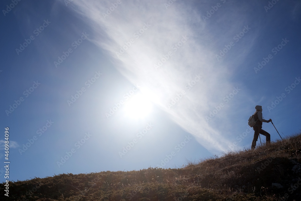Young woman hiker with backpack on top of mountain on background of blue sky. Walk in the clouds. Discovery Travel Direction Concept Young woman hiker with backpack on top of mountain on background of blue sky. Walk in the clouds. Discovery Travel Direction Concept