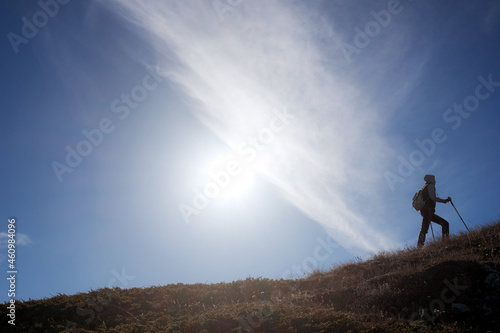Young woman hiker with backpack on top of mountain on background of blue sky. Walk in the clouds. Discovery Travel Direction Concept