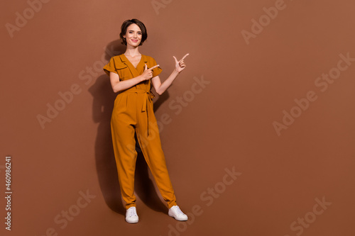 Full size photo of positive happy young woman point finger empty space choose isolated on brown color background
