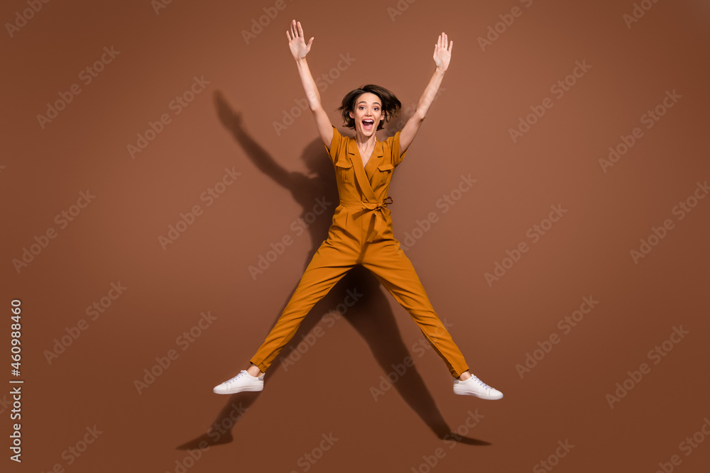 Full body photo of amazed cheerful young happy woman raise hands jump up good mood isolated on brown color background