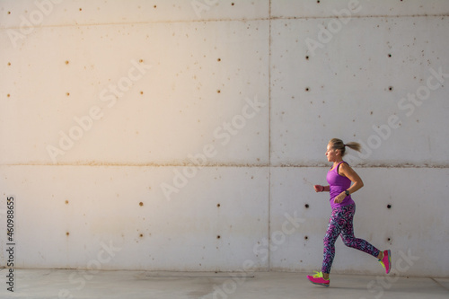 Sporty Woman. 
Beautiful Woman Running In The City Next To Buildings With Modern Architecture . Fitness, Workout, Sport, Lifestyle Concept.