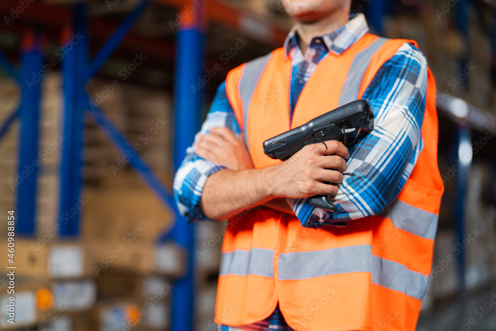 Closeup warehouse worker standing in large warehouse distribution center holding barcode reader. Closeup warehouse worker standing in large warehouse distribution center holding barcode reader.